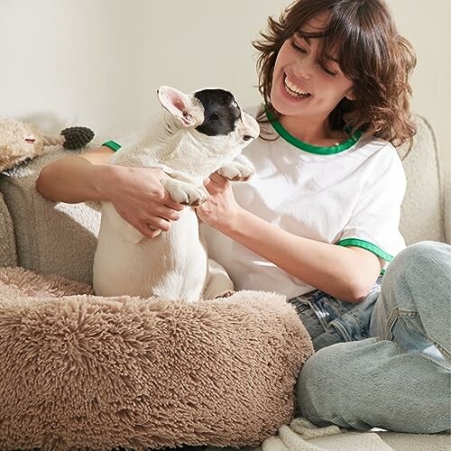 Woman smiling at a French Bulldog on a fluffy bed.